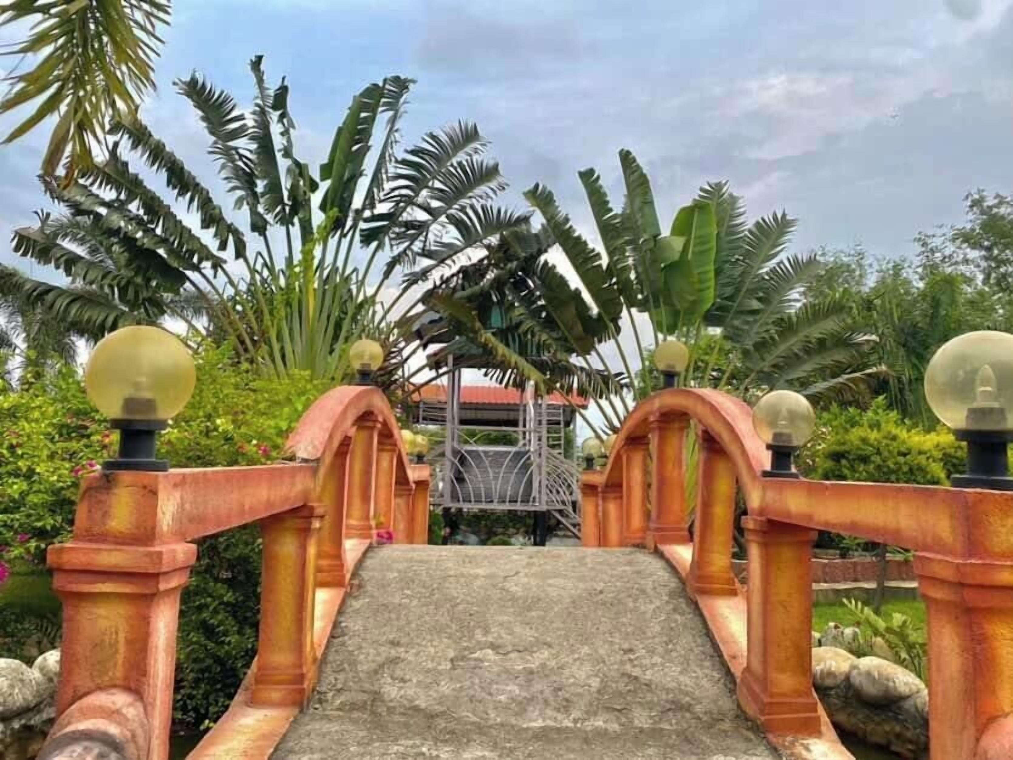 A bridge with a stone pathway leading to a structure, surrounded by lush greenery.