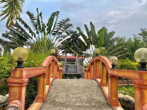 A bridge with a stone pathway leading to a structure, surrounded by lush greenery. - River View Heritage Resort Pvt. Ltd.  (Kamal)