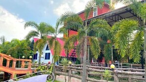 Un espace jardin agrémenté d’un banc, de palmiers et d’un bâtiment doté d’un toit rouge.