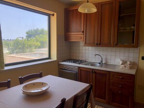 Une cuisine avec des meubles de rangement en bois, une cuisinière à gaz, un évier et une fenêtre donnant sur un espace verdoyant.