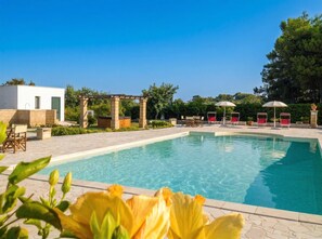 Une piscine dotée de chaises longues et d’une pergola, le tout entouré de verdure.