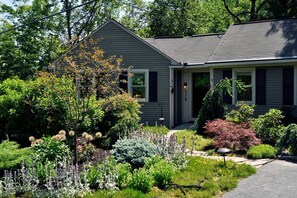 Ein Wohnhaus mit Veranda, ein gepflegter Garten mit verschiedenen Pflanzen und einem klaren Himmel.