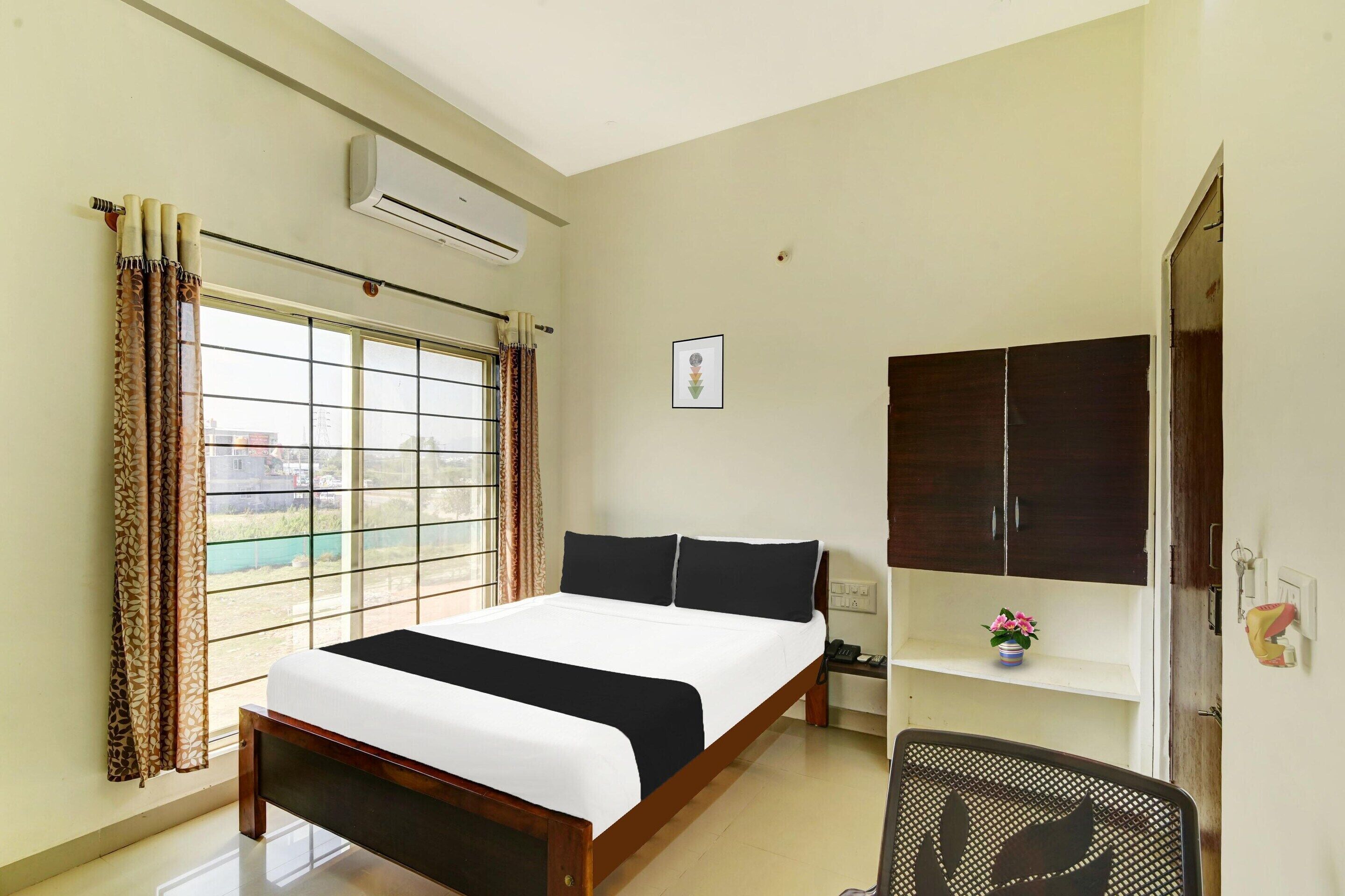 A bedroom with a bed, a desk, an air conditioner, a window with curtains, and a door.