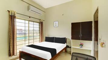 A bedroom with a bed, a desk, an air conditioner, a window with curtains, and a door.