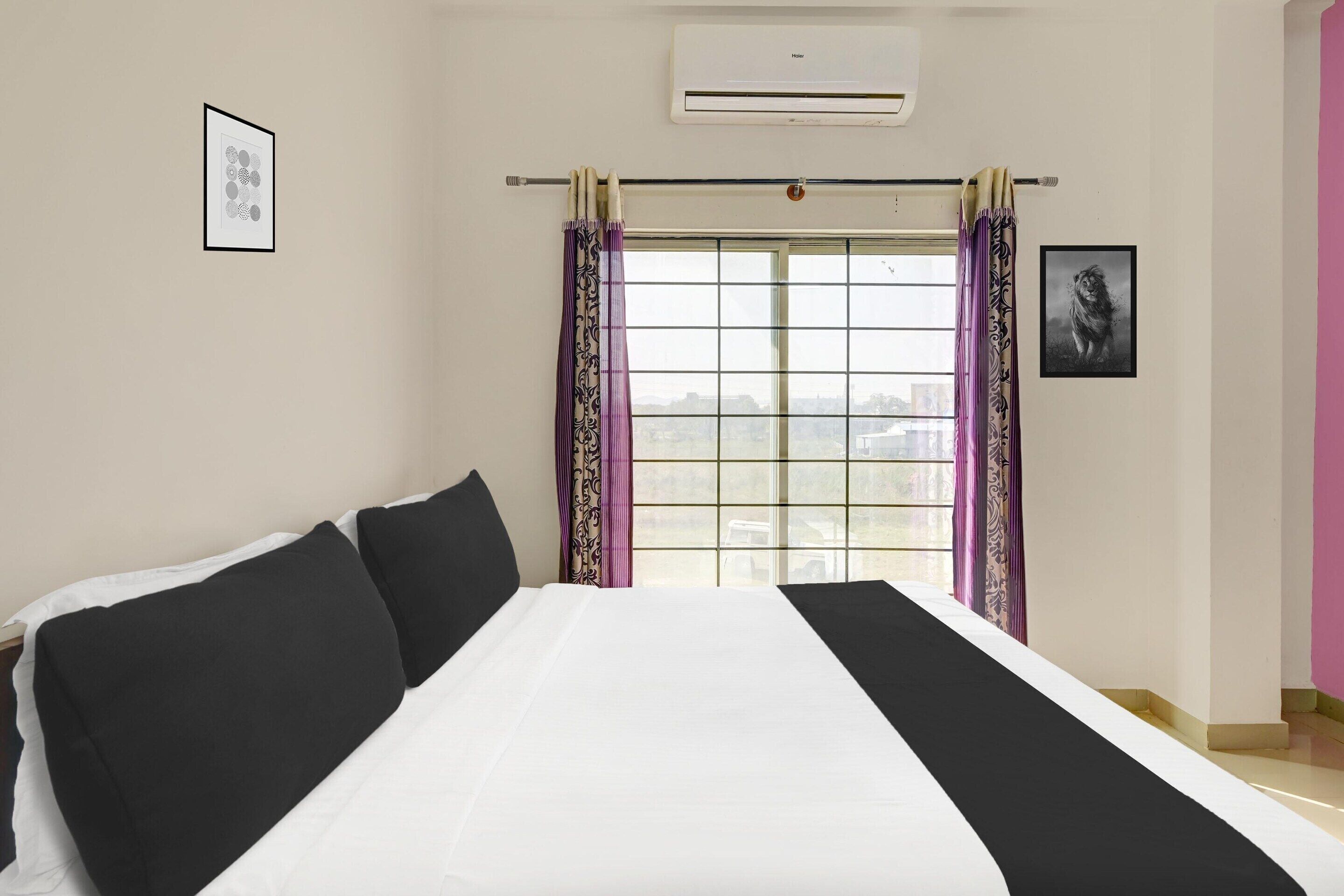 Una camera d'albergo con un letto, una finestra con tende, un condizionatore d'aria e un quadro appeso al muro.
