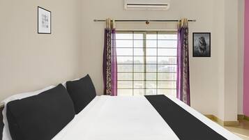 Una camera d'albergo con un letto, una finestra con tende, un condizionatore d'aria e un quadro appeso al muro.