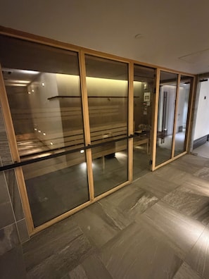 Un couloir avec des cloisons en verre, un sol carrelé et une porte donnant sur une salle de bain.