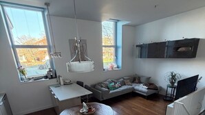 Ein modernes Wohnzimmer mit Essbereich, einer Couch, einem an der Wand montierten Fernseher und großen Fenstern.