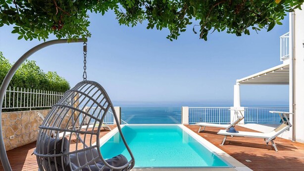 Ein Pool mit Hängesessel, Liegestuhl und Blick aufs Meer.