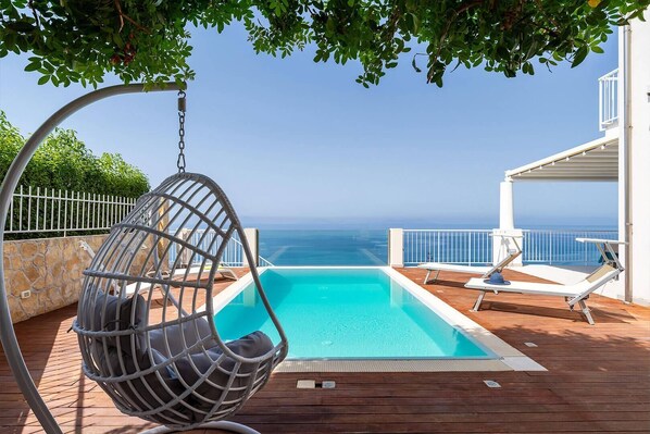Une piscine avec un fauteuil suspendu, une chaise longue et une vue sur l’océan.