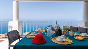 Ein Tisch ist für das Frühstück gedeckt, mit Blick auf das Meer, einem roten Hut und einem Korbwesen.
