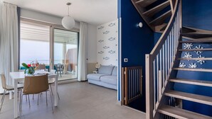 Ein modernes Wohnzimmer mit einer Couch, einem Esstisch, Stühlen, einer Treppe und Blick durch eine Glastür.