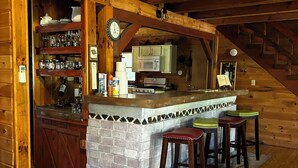 Interior de una cabaña de troncos con cocina, barra y escalera de madera.