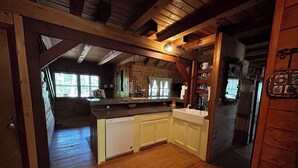 Interior de una cabaña de madera con cocina, suelo de madera y un comedor visible.