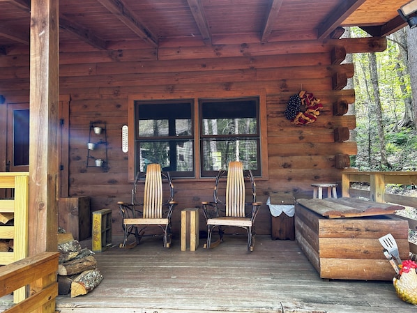 Eine Holzhütte mit zwei Schaukelstühlen, einem Holztisch und einem Fenster mit Blick auf einen Wald.