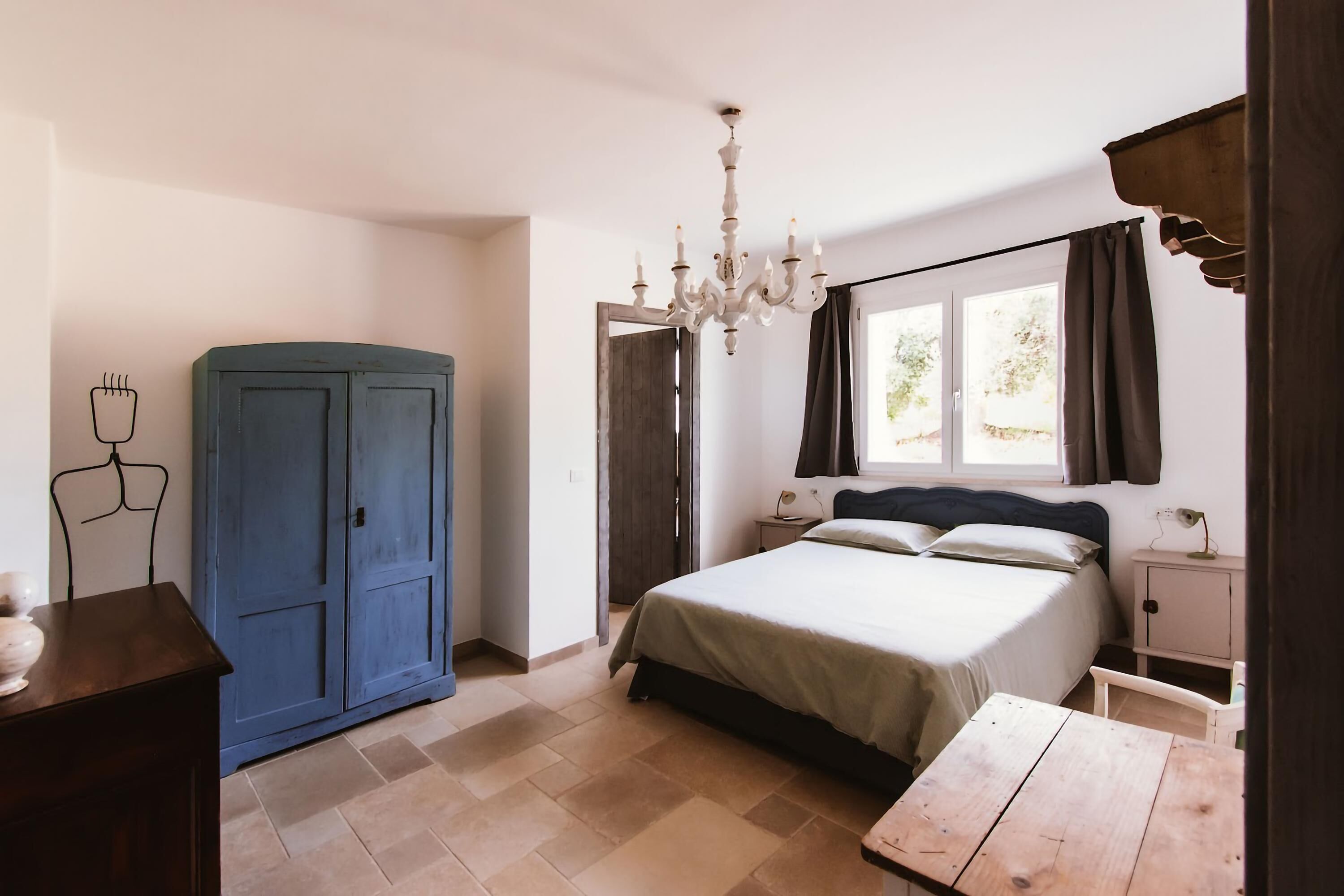 Ein Schlafzimmer mit Bett, Nachttisch, Kommode, einer Deckenleuchte und einem Fenster mit Vorhängen.