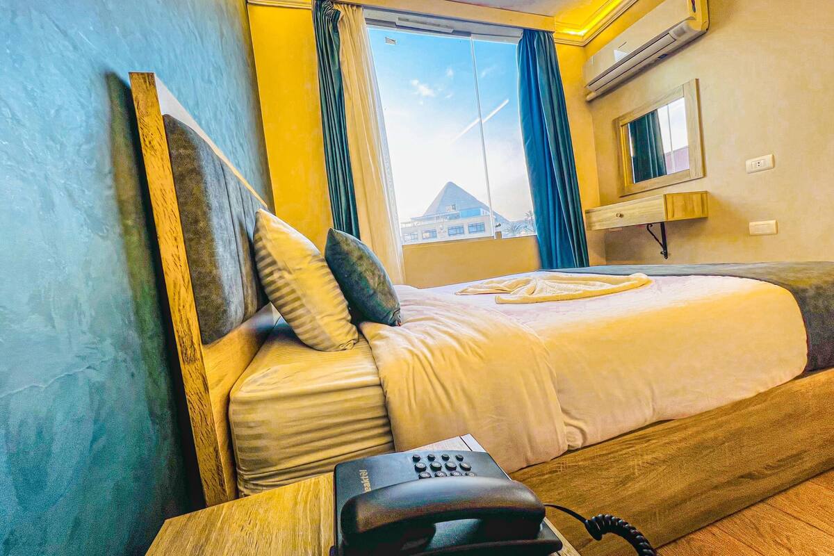 Una habitación de hotel con cama, teléfono, televisión y ventana con cortinas.