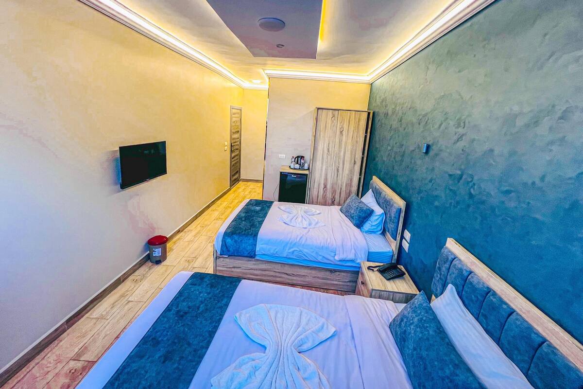 Habitación de hotel con dos camas, televisión, un escritorio pequeño con espejo y armario.