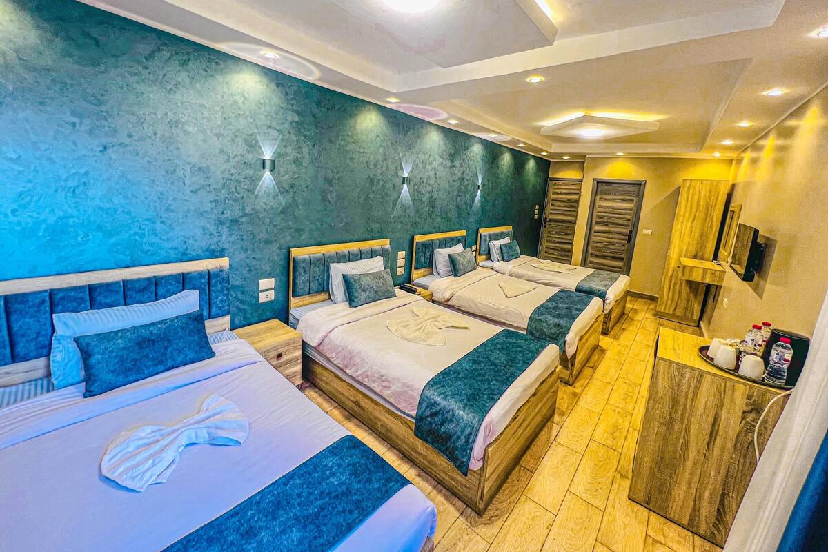 Habitación de hotel con cuatro camas, un armario de madera, un espejo y una mesita de noche con artículos de aseo.