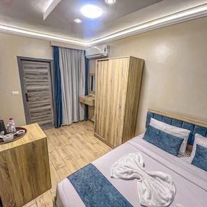 Ett hotellrum med en säng, en garderob i trä, ett skrivbord med toalettartiklar och ett badrum med duschdraperi.