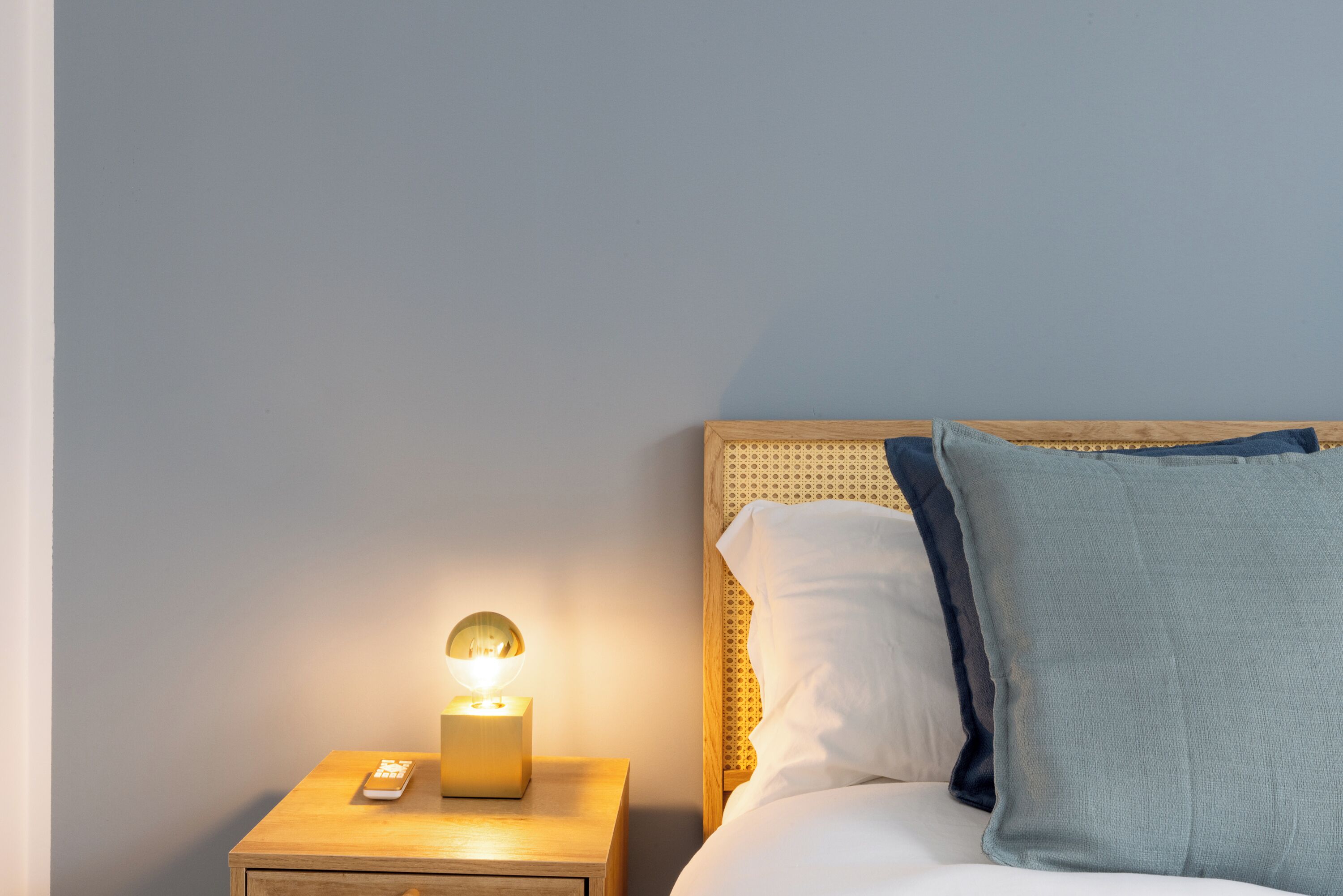 A neatly made bed with a wooden headboard, a bedside table with a lamp, and a remote control.