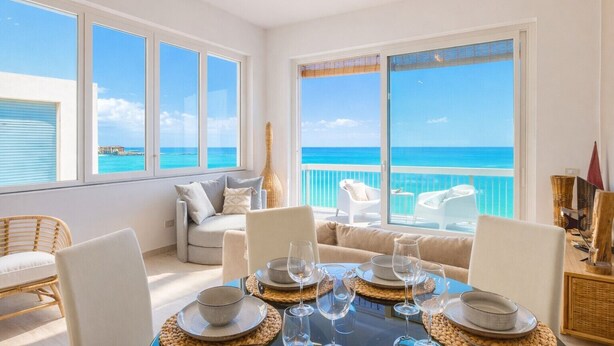 A dining area with a view of the ocean, a balcony with white furniture, and a large window. - Marzamemi on the beach SicilyMyHome (Marzamemi)