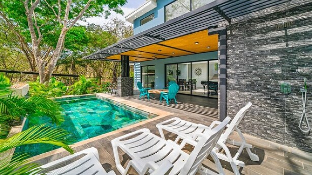 Ett modernt hus med en swimmingpool, utomhusmöbler och en täckt uteplats.