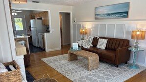 A living room with a brown sofa, a glass coffee table, a woven bench, and a patterned rug. - Steps to Beach - Prime Location Beach Bungalow – Beach Gear (Holmes Beach)