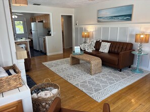 A living room with a brown sofa, a glass coffee table, a woven bench, and a patterned rug.
