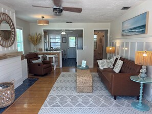 A spacious living room with a brown leather sofa, a glass coffee table, and a patterned rug.