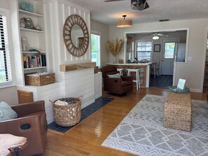 A spacious living area with a fireplace, a brown leather sofa, a wicker basket, and a kitchen in the background.