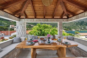 A wooden table set for breakfast with stone pillars, a view of a green landscape, and a stone wall. - Villa Royal Stone-1min walk to the Beach (Zaton)
