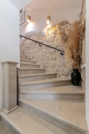 Una escalera con paredes de piedra, barandilla y un jarrón con plantas secas.