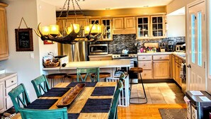 Una cocina amplia con armarios de madera, una isla central y un comedor con sillas color turquesa y una mesa de madera.