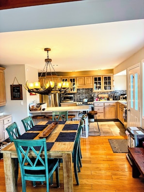 A spacious kitchen with wooden cabinets, a central island, and a dining area with teal chairs and a wooden table.