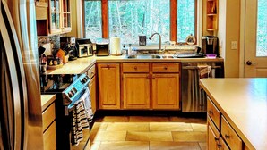 Una cocina con armarios de madera, un refrigerador de acero inoxidable, un horno empotrado y una ventana con vista a árboles.