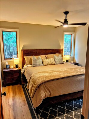A bedroom with a wooden headboard, a bed with multiple pillows, two bedside tables with lamps, and a ceiling fan.