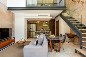 Ein modernes Wohnzimmer mit Sofa, Esstisch, Stühlen, Fernseher und einer Treppe.