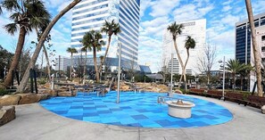 Ein öffentlicher Park mit blau-kariertem Boden, Palmen und modernen Gebäuden im Hintergrund.
