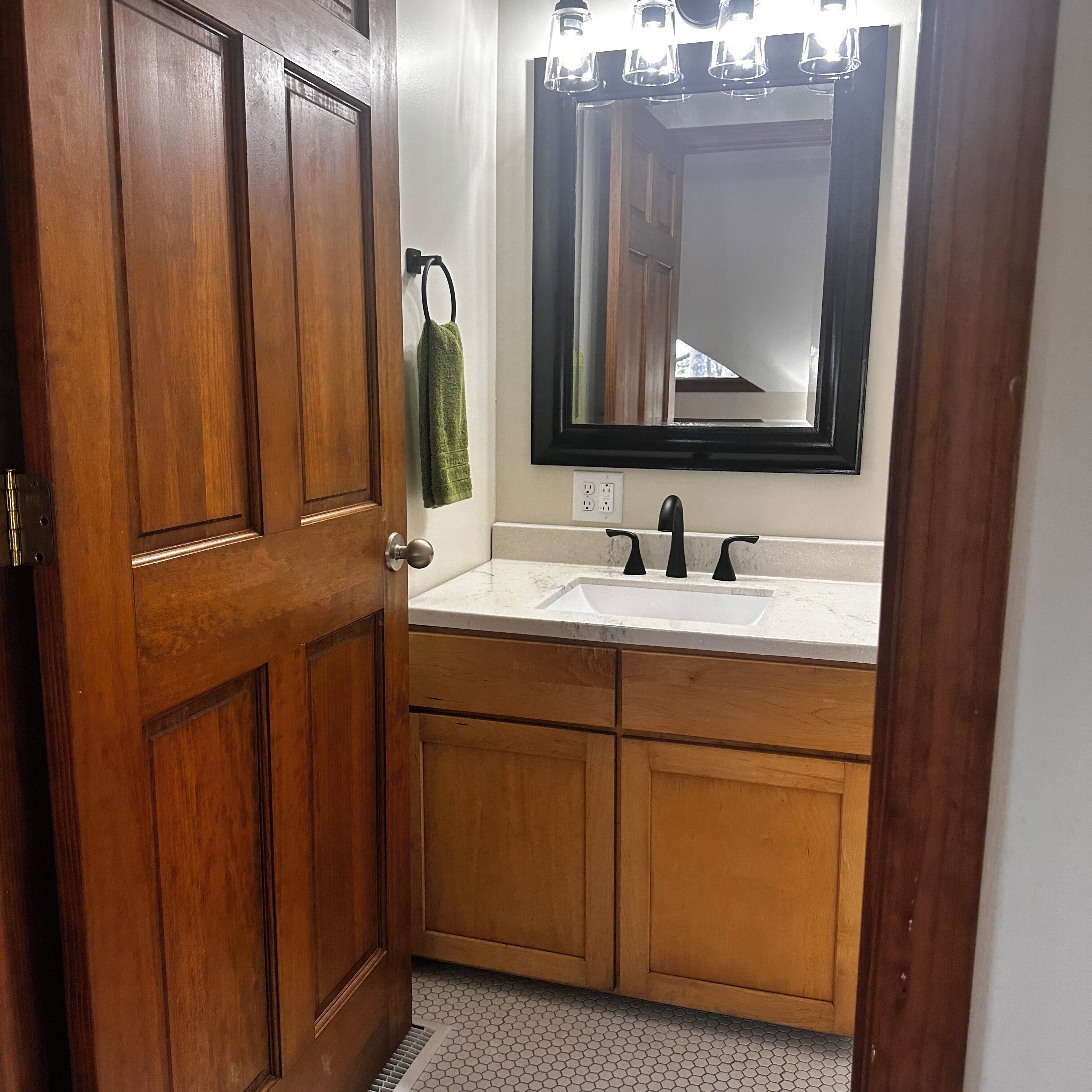 A bathroom with a wooden door, a white sink, a mirror, and a towel hanging on the wall.