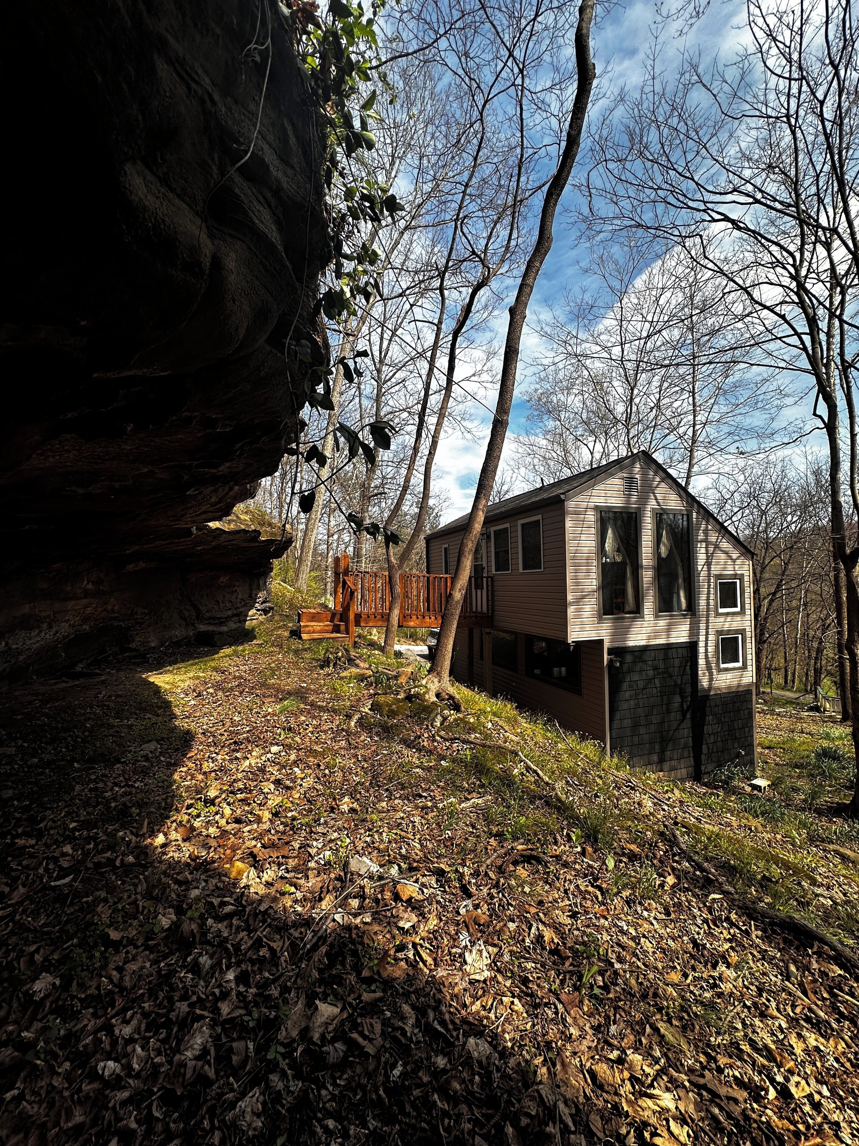 A cabin with a stone foundation, a wooden deck, and a view of the surrounding forest.