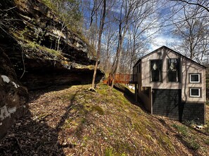 Eine Holzhütte mit Steinunterbau, einer Holzdiele und Blick auf ein bewaldetes Gebiet.