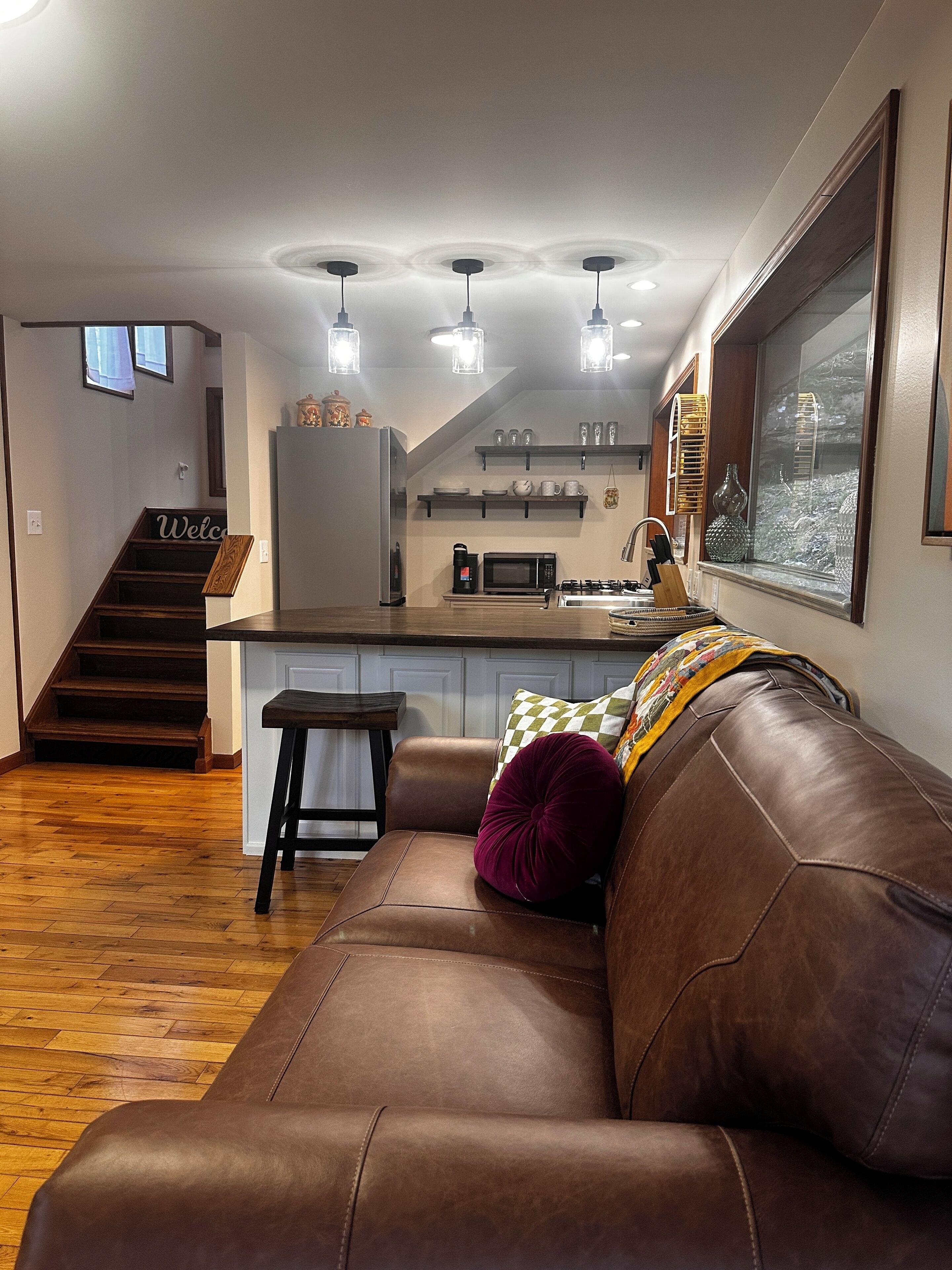 Eine moderne Küche mit einer zentralen Kochinsel, einer Holztreppe und einem Ledersofa mit Kissen.