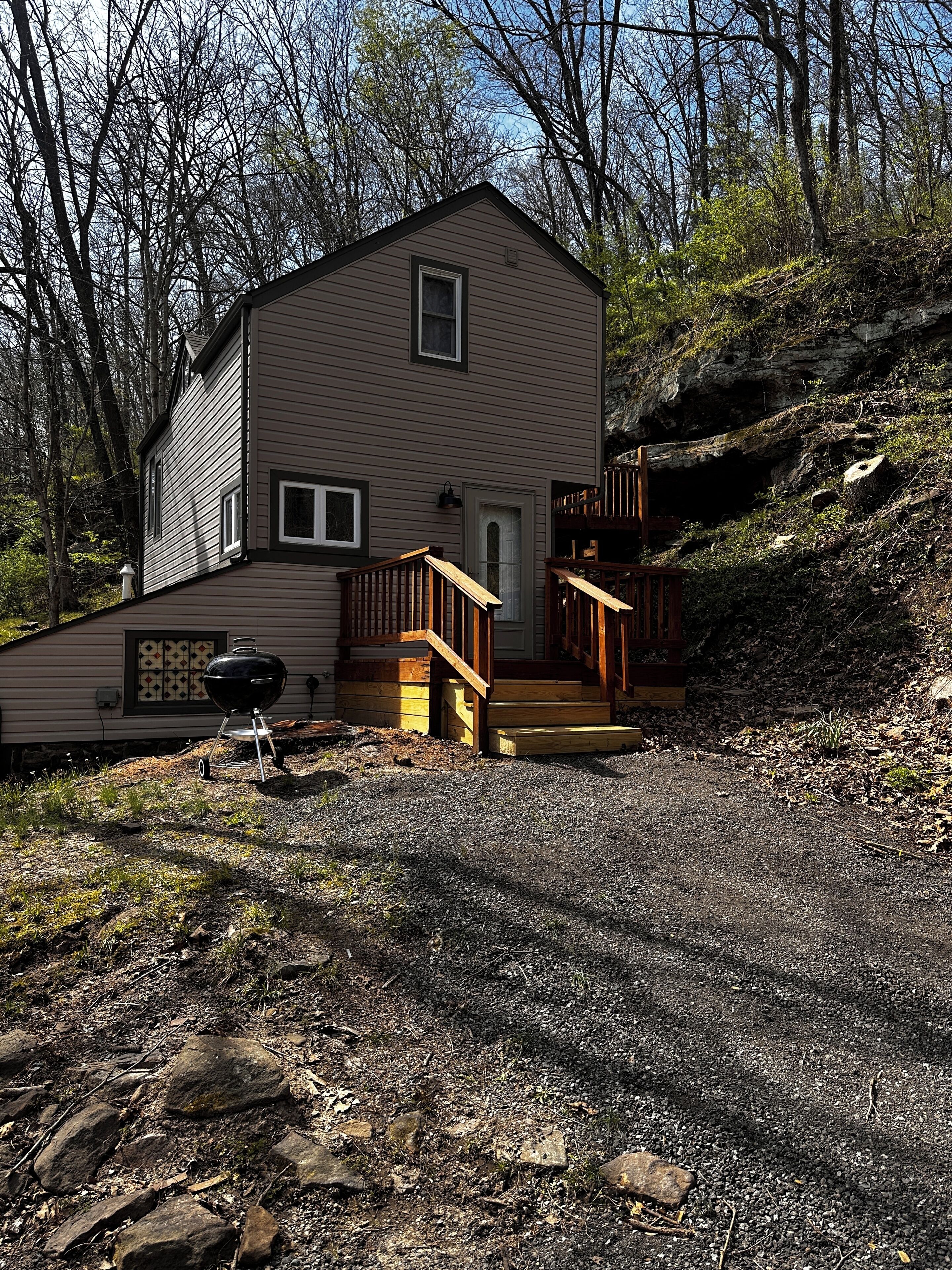 Une cabane à deux étages avec un porche à l’avant, un petit barbecue extérieur et un escalier menant à l’entrée.