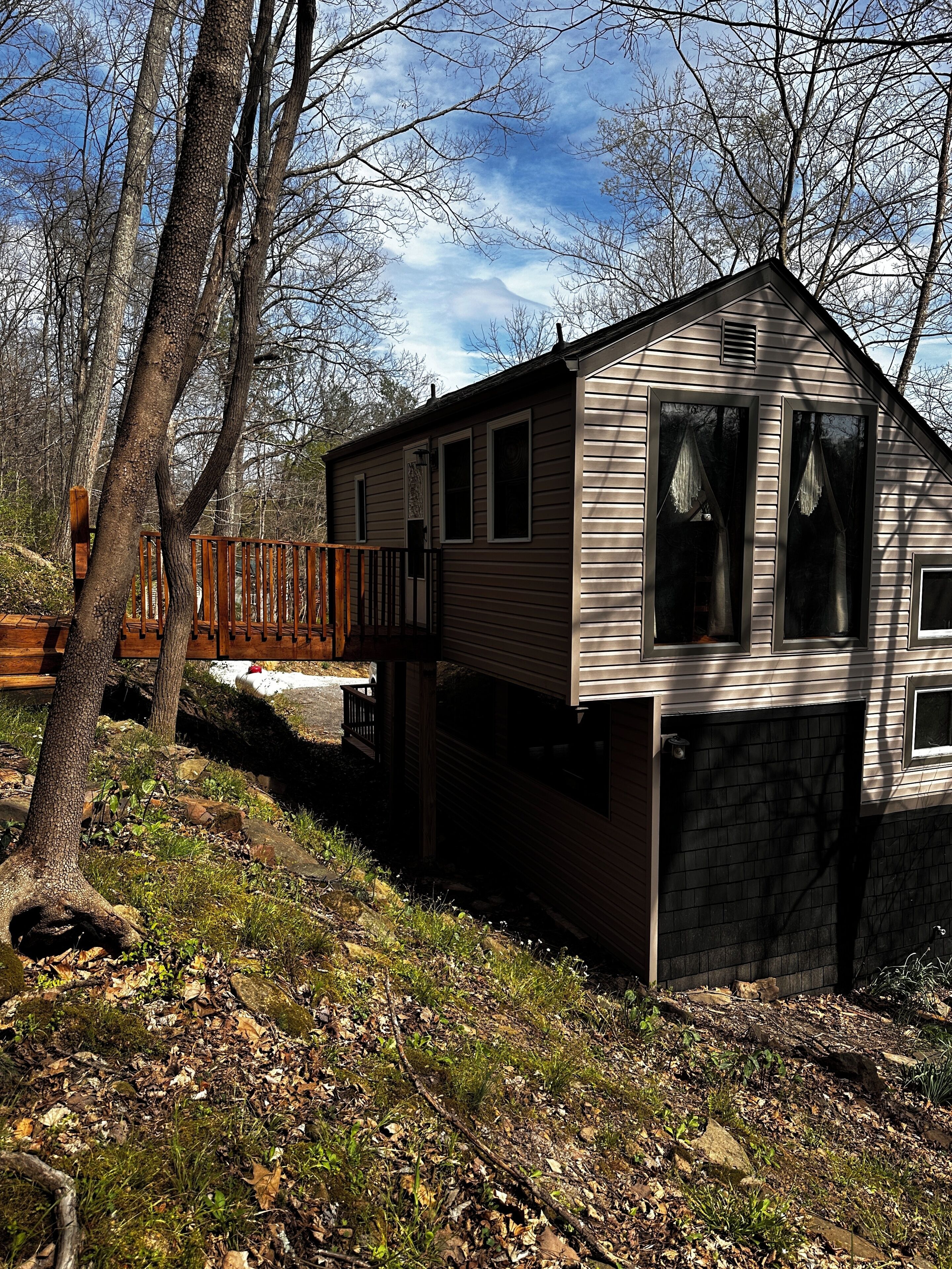 A single-story cabin with a stone foundation, a wooden deck, and a view of a mountain.