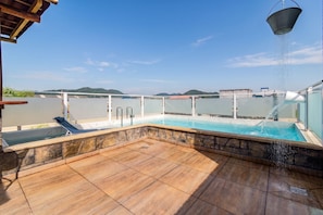 Uma piscina no terraço com borda de pedra, uma espreguiçadeira e vista para colinas ao longe.