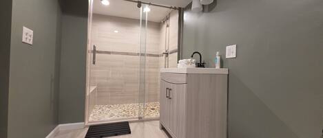 Une salle de bain moderne équipée d’une douche, d’un lavabo avec des articles de toilette et d’un luminaire.