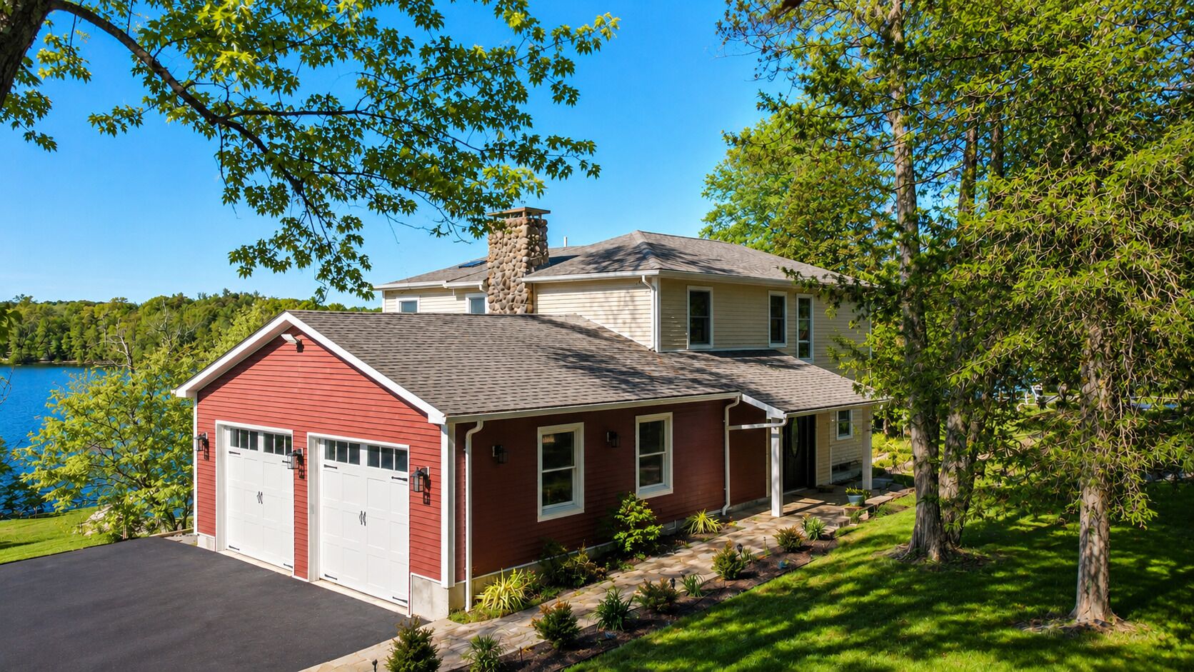 Une maison à deux étages avec un garage, une cheminée et une vue sur un lac.