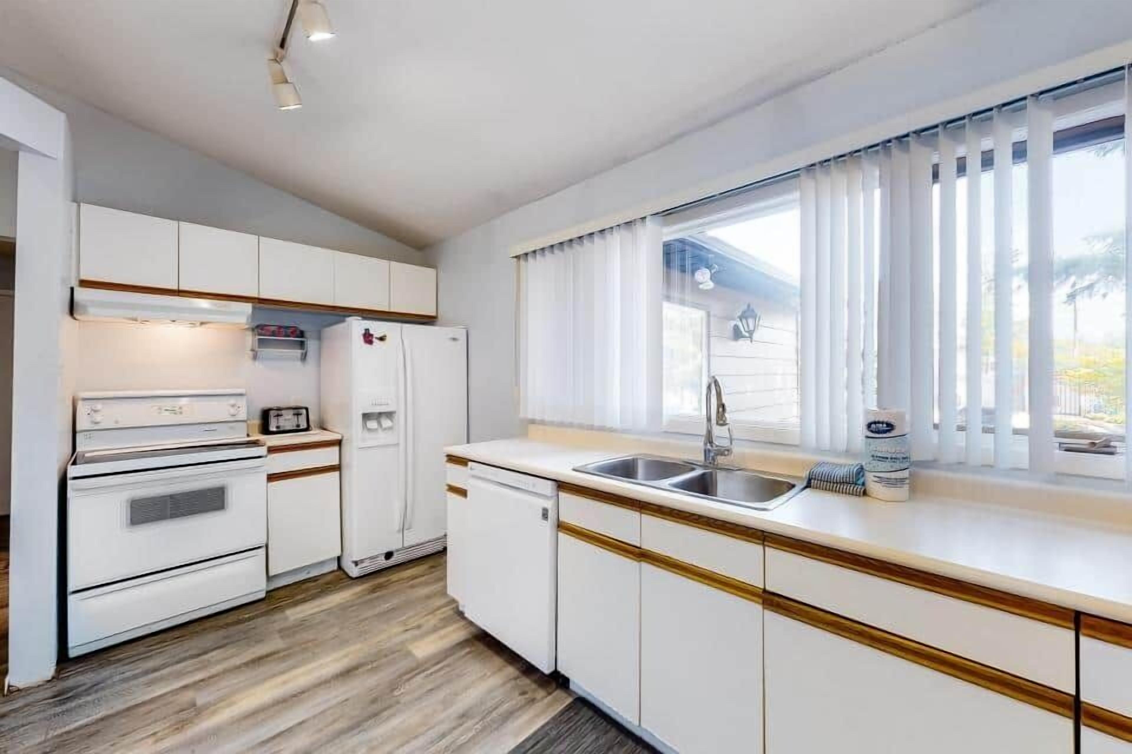 Eine kleine Küche mit weißen Schränken, einem eingebauten Ofen, einem Kühlschrank und einer Spüle.
