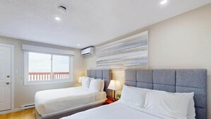 Hotelkamer met twee bedden, een raam met uitzicht, een wandairconditioner en een modern kunstwerk.